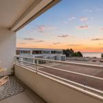 Balcony with table and chairs overlooking sea at sunset.
