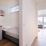 Bedroom with bed, nightstand, and picture. Passage to living area with balcony.
