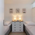 Two single beds flank a dresser with two lamps and three pictures on the wall.