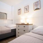 Two beds with white pillows and light bedspreads. Between them stands a dresser with two lamps.