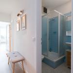 Hallway with stool and pictures, bathroom with shower and blue tiles.