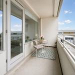 Balcony with table, chairs, and flowers. View of the sea and buildings.