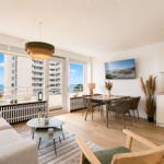 Living area with dining space, balcony, and sea view. Modern furnishings and bright ambiance.