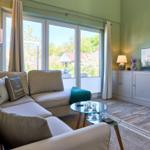 Wohnzimmer mit Sofa, Glas-Tisch und TV. Große Fenster mit Blick auf Garten.
