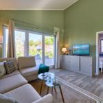 Wohnzimmer mit Sofa, Glas-Tisch und TV. Durchgang zu Schlafzimmer mit blauer Wand.