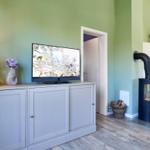 Ein Wohnzimmer mit Fernseher, Kaminofen und Holzoptikfußboden.