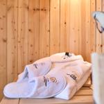 Weißer Bademantel und Hausschuhe liegen auf einer Holzbank in einer Sauna.