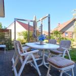 Terrasse mit weißem Tisch, Stühlen und Sonnenschirm. Hintergrund: Garten und Nachbarhäuser.