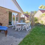 Terrasse mit Gartenhaus, Tisch, Stühlen und Liegestuhl. Blick auf grünen Rasen und blühende Sträucher.