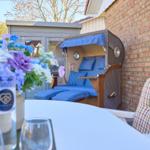 Terrasse mit Strandkorb, Tisch, Stühlen und Blumenarrangement.