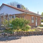 Ein kleines Haus mit Steinmauer, Garten und Terrasse unter blauem Himmel.
