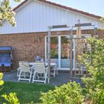 Terrasse mit Tisch, Stühlen und Sonnenschutz neben Haus mit Ziegelwand und weißen Holzverkleidungen.