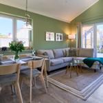 Wohn- und Essbereich mit Sofa, Tisch und Stühlen. Grüne Wände und große Fenster.