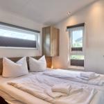 Schlafzimmer mit Doppelbett, zwei Fenstern und Holzmöbeln.