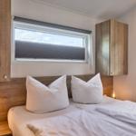 Schlafzimmer mit Doppelbett, zwei Fenstern und Holzregalen an den Wänden.