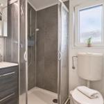 Badezimmer mit Dusche, Waschbecken und Toilette. Fenster mit Pflanze.