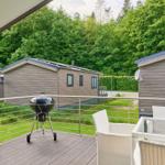 Terrasse mit Grill und Sitzgelegenheiten, Blick auf Ferienhäuser und grüne Bäume.