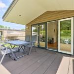 Terrasse mit Tisch, Stühlen und Grill. Durchgehende Glastüren führen ins Innere.