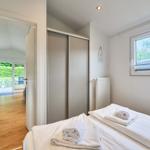 Schlafzimmer mit Bett, Kleiderschrank und Fenster. Durchgang zu Wohnbereich mit Holzboden.
