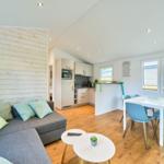 Wohnzimmer mit Sofa, Essbereich und Küchenzeile. Holzwand, Holzboden und Fenster.