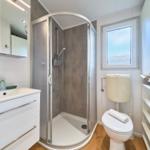 Badezimmer mit Dusche, Waschbecken und Toilette. Fenster mit getöntem Glas.