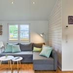 Ein Wohnbereich mit grauem Sofa, zwei runden Tischen und einem Fenster.