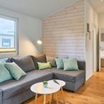 Wohnzimmer mit Sofa, Tisch und Fenster. Im Hintergrund ist ein Schlafzimmer sichtbar.