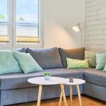 Ein grauer Sofa mit grünen Kissen und einem runden Tisch vor einem Fenster.