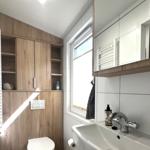 Badezimmer mit Holzschränken, Waschbecken und Fenster.