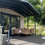 Terrasse mit Sitzgruppe unter Markise, umgeben von Wald.