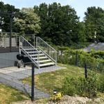 Terrasse mit Stufen, Grill und Gartenzaun. Hintergrund: Bäume und Solaranlage.