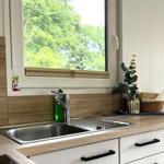 Küchenzeile mit Spüle, Fenster und Pflanze. Holzoptik und weiße Schränke.