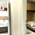 Zimmer mit zwei Betten und Holzmöbeln. Tür führt zu einem Schlafzimmer.