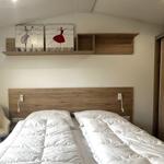 Schlafzimmer mit Doppelbett, Holzkopfteil, Wandregal und Stuhl.