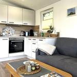 Küche mit Schränken, Herd und Fenster. Wohnbereich mit Sofa und Tisch.