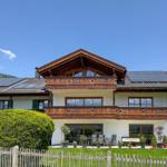 Haus mit Balkonen, Solaranlagen und Garten. Berglandschaft im Hintergrund.