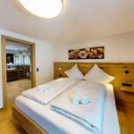 Schlafzimmer mit Holzbett und Bad im Hintergrund.