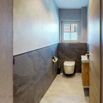Badezimmer mit Toilette, Waschbecken und Fenster. Wandverkleidung aus Stein und Holz.