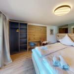 Schlafzimmer mit Doppelbett, Kleiderschrank und Schreibtisch. Holzboden und große Fenster.