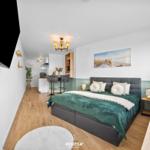 Schlafzimmer mit Bett, TV und Küchenbereich im Hintergrund.