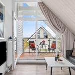 Wohnbereich mit Balkon, Sofa und Fernseher. Blick auf Haus und Strand.