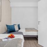Zwei Betten mit Kissen und Decken, Wandbild mit Muscheln, Tür und Holzboden.