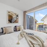 Schlafzimmer mit großem Bett und Blick auf Balkon mit Tisch und Stühlen.