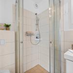 Badezimmer mit Dusche, Waschbecken und Toilette. Weiße Fliesen und Glaswand.