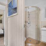 Badezimmer mit Dusche, Waschbecken und Spiegel. Blick in Schlafzimmer mit Bett und Wandbild.