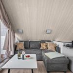 Wohnbereich mit grauem Sofa, Couchtisch und Holzdecke. Große Fenster mit Blick auf Balkon.