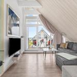 Wohnzimmer mit Sofa, Fernseher und Kamin. Durchgang zum Balkon mit Sicht auf Haus und Meer.