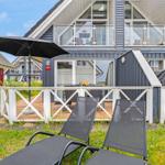 Haus mit Terrasse, Liegestühlen und Sonnenschirm. Zwei Etagen mit Balkon und Fenstern.