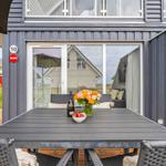 Terrasse mit Tisch, Stühlen und Blumen vor einem Haus mit Glasfront.