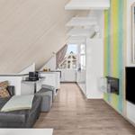 Wohnbereich mit Sofa, Küchenzeile und Fernseher unter schrägem Dach